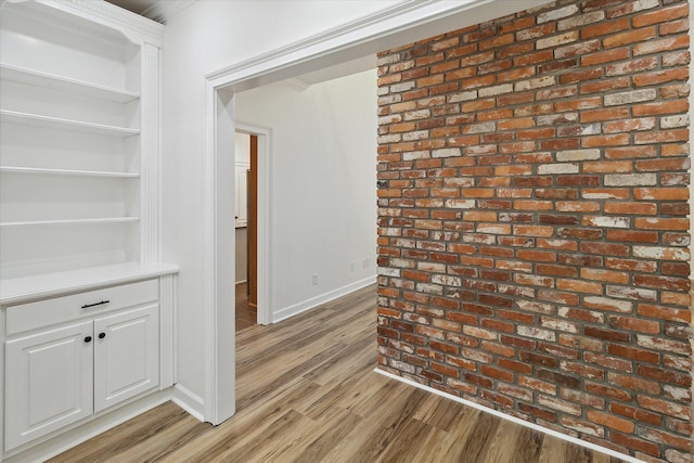 hall featuring baseboards, brick wall, and light wood-style flooring