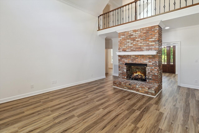 unfurnished living room with wood finished floors, a fireplace, baseboards, a high ceiling, and crown molding