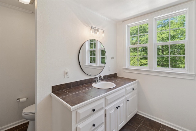 bathroom with vanity, toilet, crown molding, baseboards, and tile patterned flooring