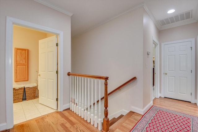 corridor featuring visible vents, ornamental molding, light wood finished floors, and an upstairs landing