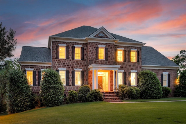 colonial inspired home featuring brick siding, a front yard, and roof with shingles