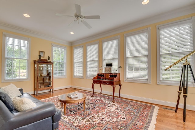 living area with crown molding, ceiling fan, baseboards, and light wood-style floors