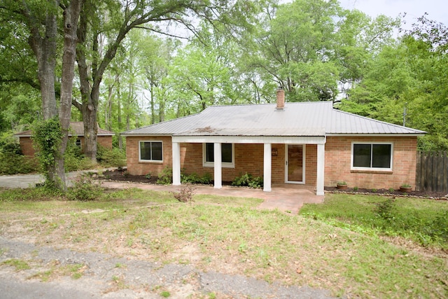 rear view of house featuring brick siding, fence, a chimney, and metal roof