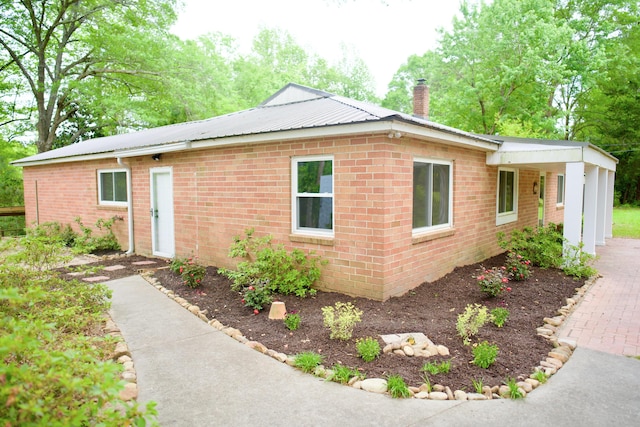 view of front of home with brick siding, a chimney, and metal roof