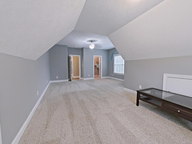 bonus room featuring lofted ceiling, light colored carpet, and a textured ceiling