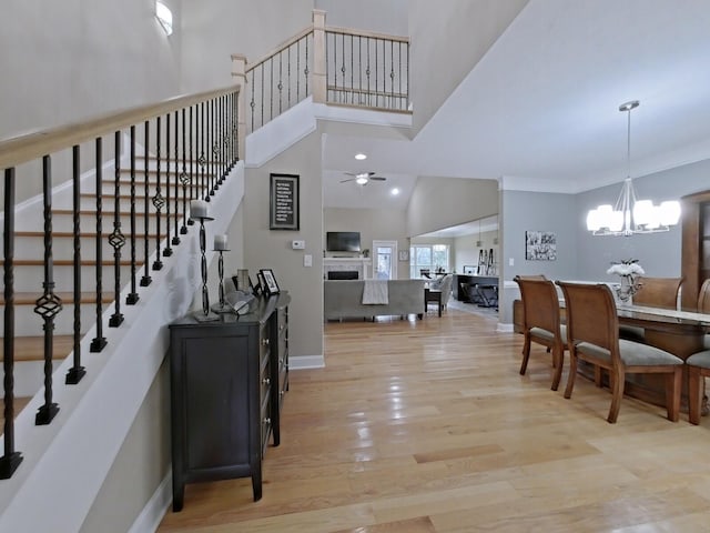 interior space with a towering ceiling, ceiling fan with notable chandelier, light hardwood / wood-style floors, and ornamental molding