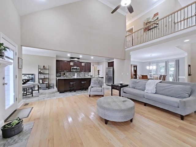 living room featuring ceiling fan with notable chandelier, light wood-type flooring, crown molding, and high vaulted ceiling