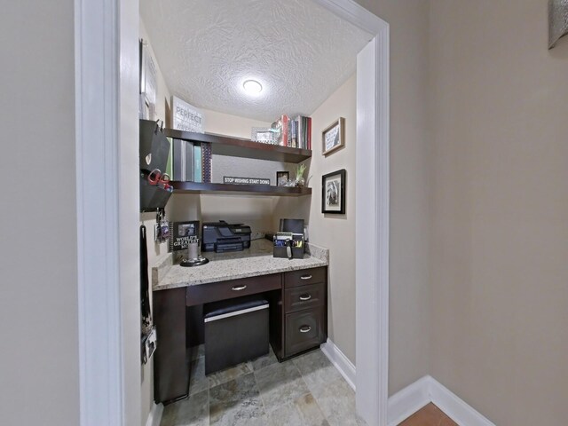 office with built in desk and a textured ceiling