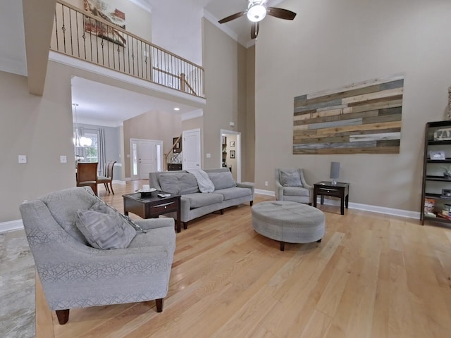 living room with ceiling fan with notable chandelier, light wood-type flooring, ornamental molding, and a high ceiling