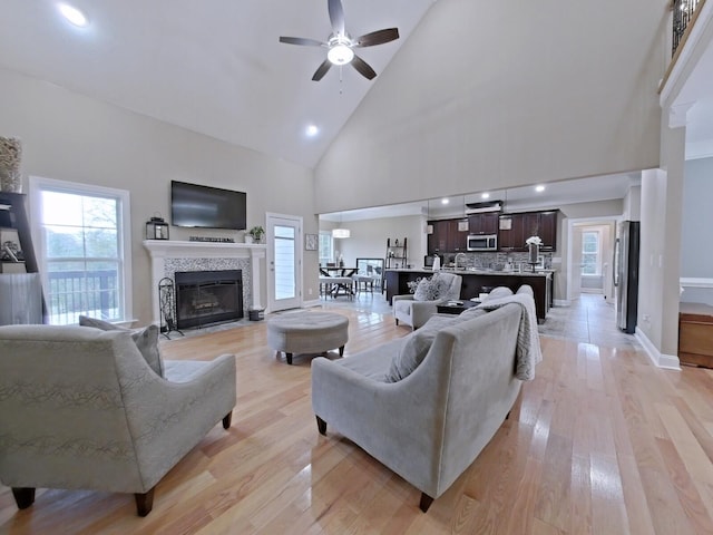 living room with a tile fireplace, ceiling fan, a healthy amount of sunlight, light hardwood / wood-style flooring, and high vaulted ceiling