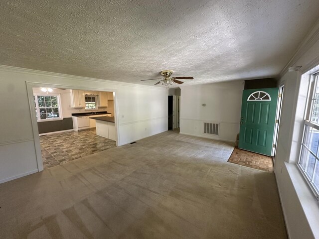 unfurnished living room featuring a textured ceiling, ceiling fan, carpet flooring, and crown molding