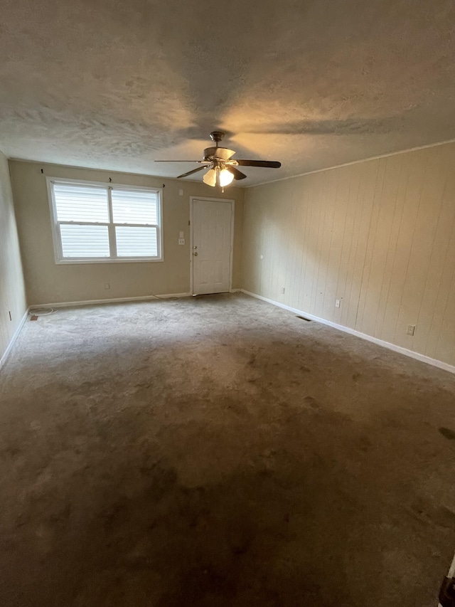 carpeted spare room with a textured ceiling, ceiling fan, and wood walls