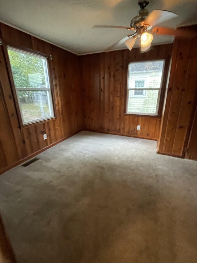 carpeted empty room with ceiling fan and wooden walls