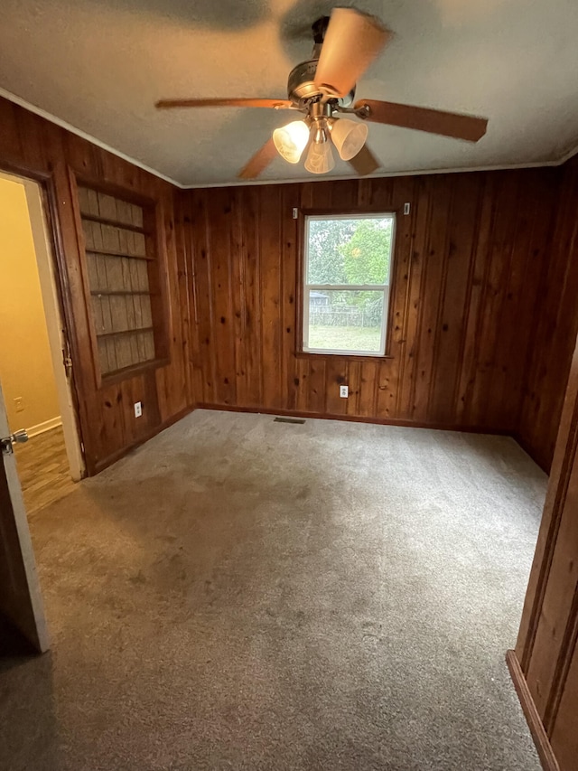 empty room featuring light carpet, wooden walls, ceiling fan, and ornamental molding