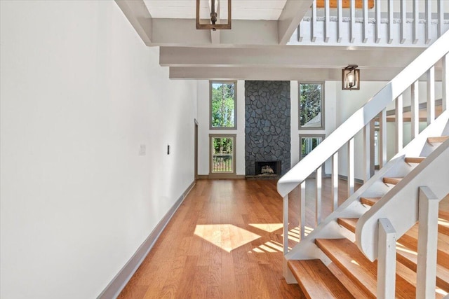 entryway with wood finished floors, a stone fireplace, stairway, and baseboards