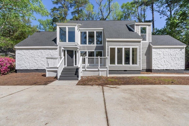 view of front of property with crawl space, a deck, stone siding, and a shingled roof