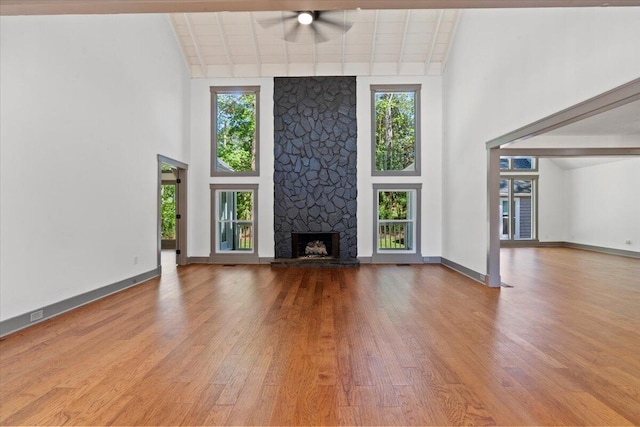 unfurnished living room featuring a ceiling fan, a high ceiling, healthy amount of natural light, wood finished floors, and a stone fireplace