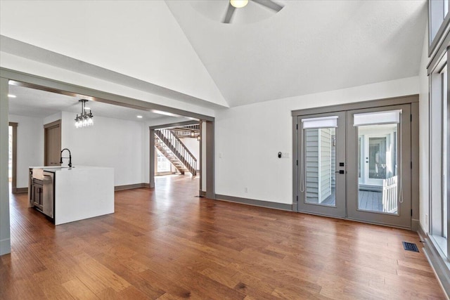 unfurnished living room with stairs, ceiling fan, dark wood-style flooring, a chandelier, and high vaulted ceiling