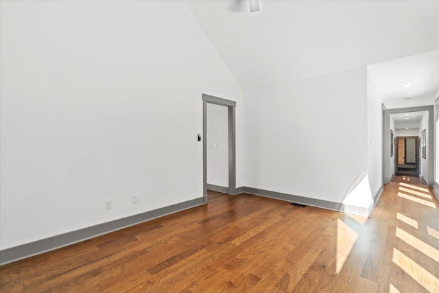 unfurnished room featuring wood finished floors, baseboards, and lofted ceiling