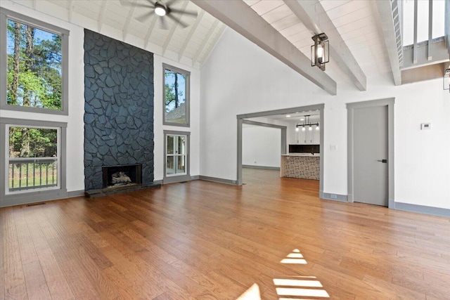 unfurnished living room with high vaulted ceiling, a stone fireplace, a ceiling fan, beam ceiling, and wood finished floors
