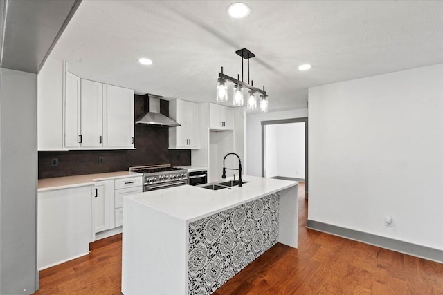 kitchen with wall chimney range hood, a sink, stainless steel stove, white cabinetry, and recessed lighting