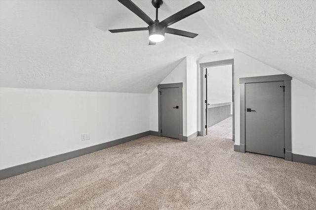 additional living space featuring a textured ceiling, carpet flooring, ceiling fan, vaulted ceiling, and baseboards