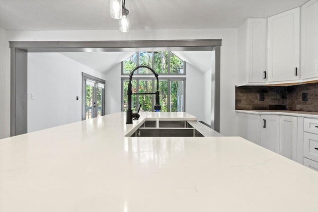 kitchen with a sink, lofted ceiling, white cabinets, backsplash, and healthy amount of natural light