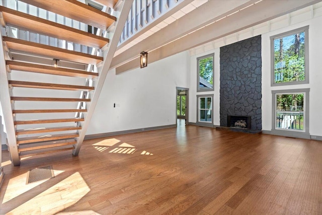 unfurnished living room with a high ceiling, plenty of natural light, a fireplace, wood finished floors, and stairs
