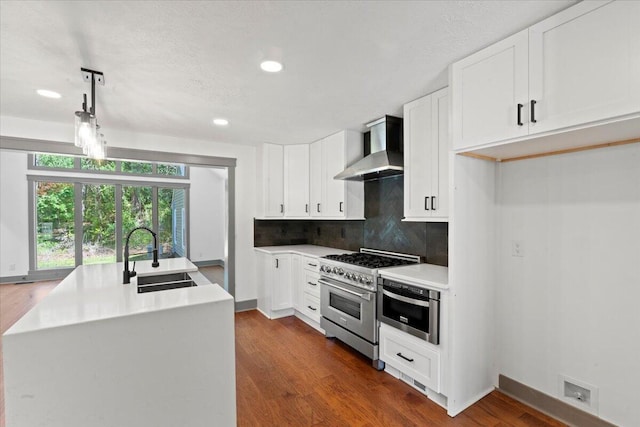 kitchen featuring a sink, wall chimney range hood, stainless steel stove, tasteful backsplash, and dark wood-style flooring