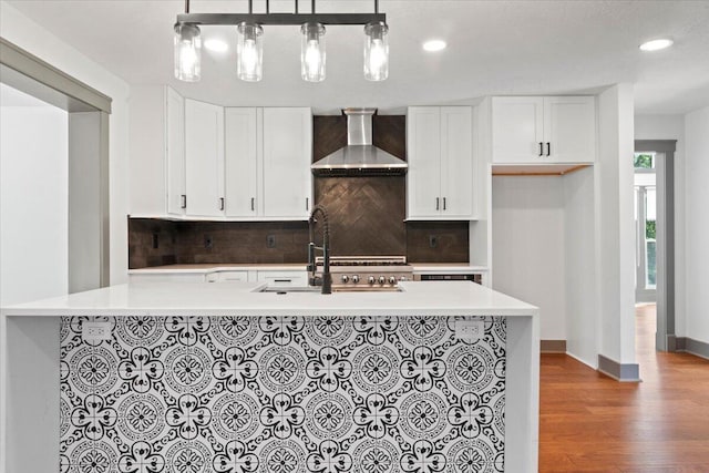 kitchen featuring wall chimney exhaust hood, a sink, tasteful backsplash, wood finished floors, and light countertops