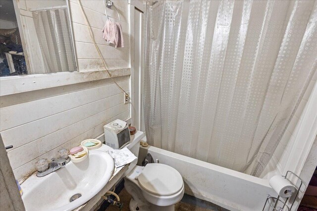 full bathroom featuring wood walls, toilet, sink, and shower / tub combo