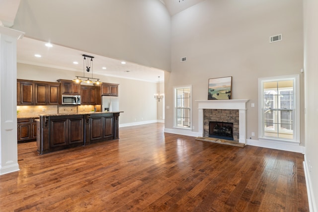 kitchen with white fridge with ice dispenser, hanging light fixtures, a high ceiling, a stone fireplace, and a kitchen island with sink