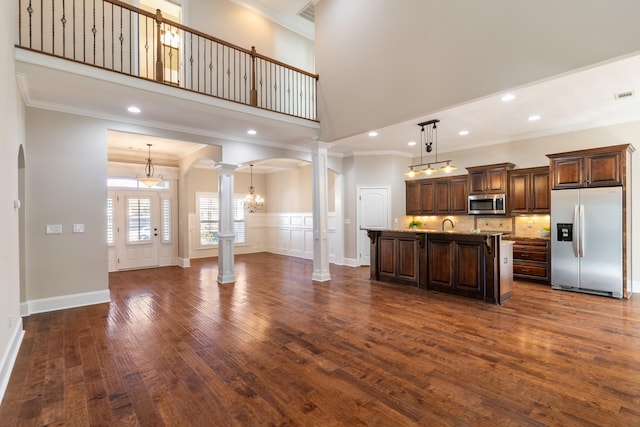 kitchen with ornate columns, stainless steel appliances, a high ceiling, pendant lighting, and a center island with sink