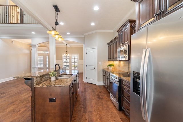 kitchen featuring ornate columns, sink, an island with sink, pendant lighting, and appliances with stainless steel finishes