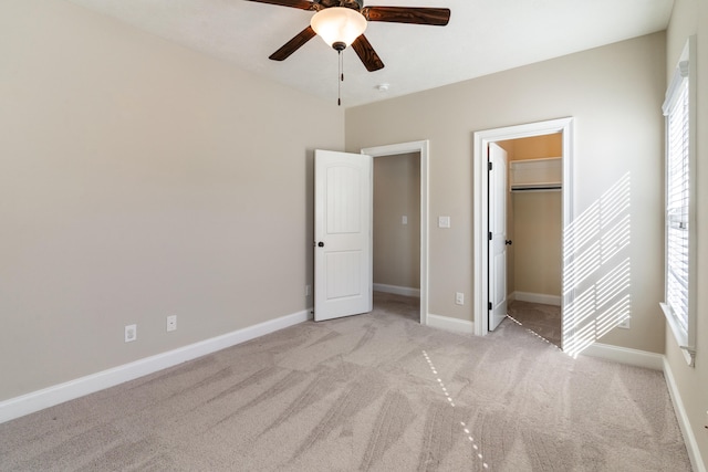 unfurnished bedroom featuring ceiling fan, light colored carpet, a walk in closet, and a closet