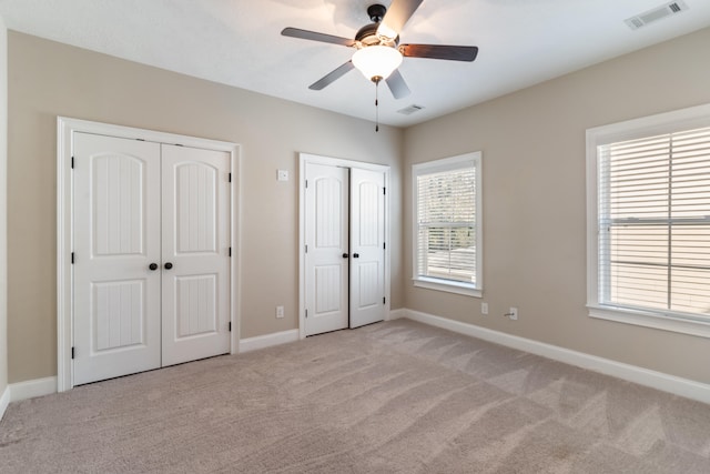 unfurnished bedroom with ceiling fan, light carpet, and two closets