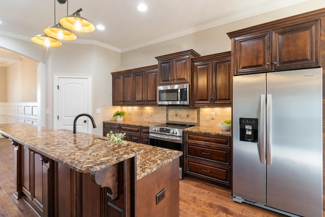 kitchen featuring light stone countertops, hanging light fixtures, stainless steel appliances, a kitchen bar, and a center island with sink