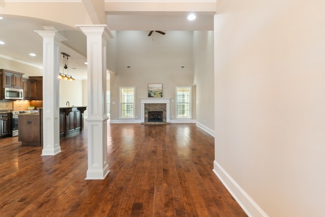 unfurnished living room featuring a fireplace, dark hardwood / wood-style flooring, ornate columns, and ceiling fan