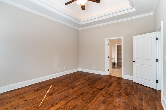 empty room with ceiling fan, a raised ceiling, crown molding, and dark wood-type flooring