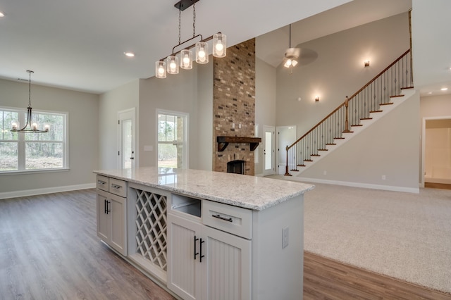 kitchen featuring ceiling fan with notable chandelier, light stone countertops, decorative light fixtures, a large fireplace, and white cabinetry