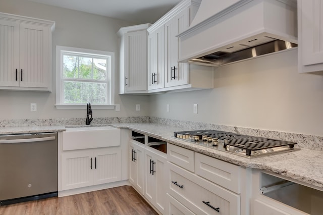 kitchen with premium range hood, white cabinets, sink, light stone countertops, and appliances with stainless steel finishes