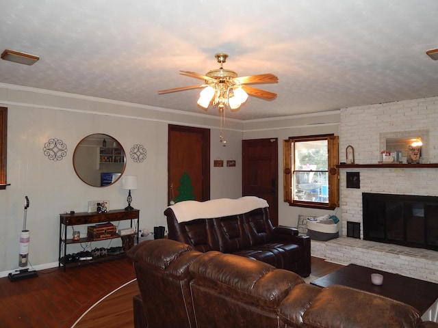 living room with dark wood-type flooring, crown molding, ceiling fan, a textured ceiling, and a fireplace