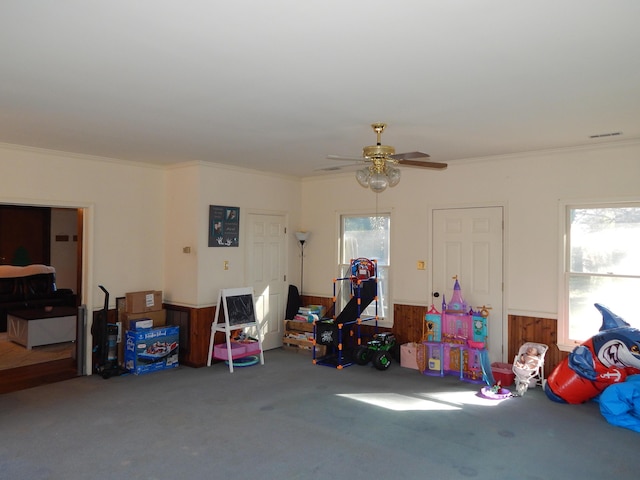 recreation room with carpet, ceiling fan, crown molding, and wooden walls