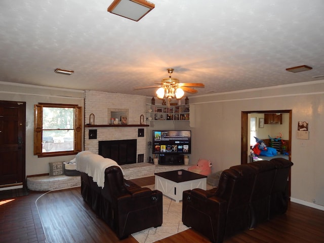 living room featuring ceiling fan, a brick fireplace, hardwood / wood-style floors, a textured ceiling, and ornamental molding