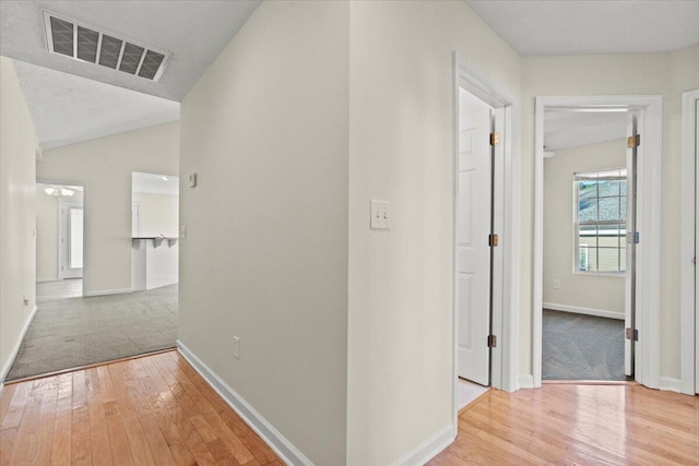 hall with a textured ceiling, light hardwood / wood-style floors, and lofted ceiling