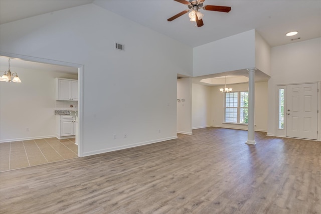 unfurnished living room with a chandelier, high vaulted ceiling, ornate columns, ceiling fan, and light wood finished floors