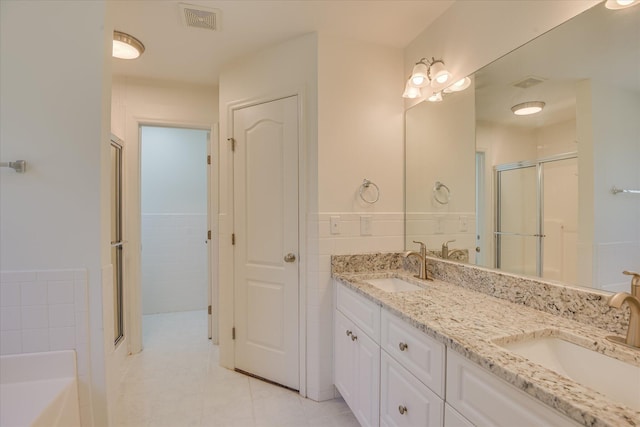 bathroom with a stall shower, double vanity, wainscoting, tile patterned flooring, and a bathtub