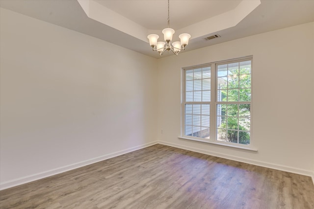 unfurnished room with a tray ceiling, wood finished floors, baseboards, and a chandelier