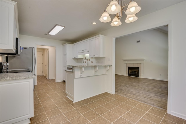 kitchen with white cabinets, a chandelier, a peninsula, a kitchen bar, and light stone counters