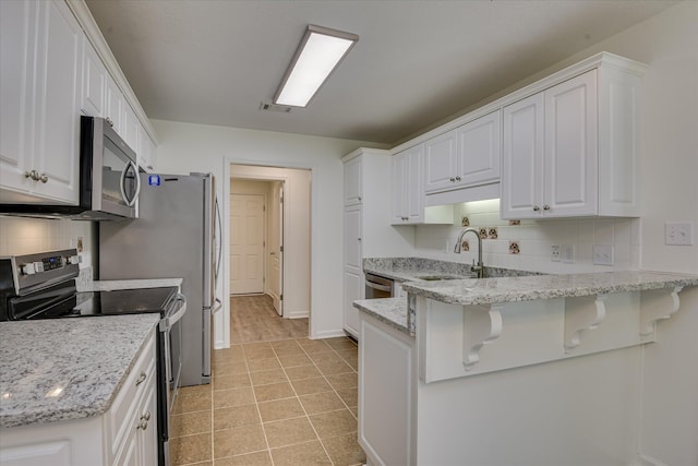 kitchen with stainless steel appliances, a sink, white cabinets, backsplash, and a peninsula